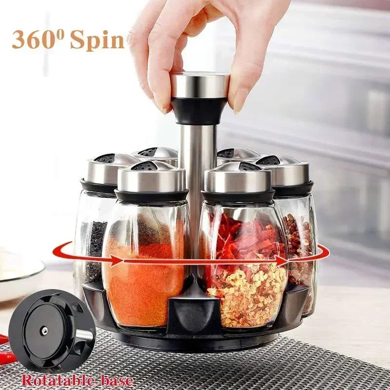 A hand is rotating a set of glass spice jars with black lids and a rotating base.