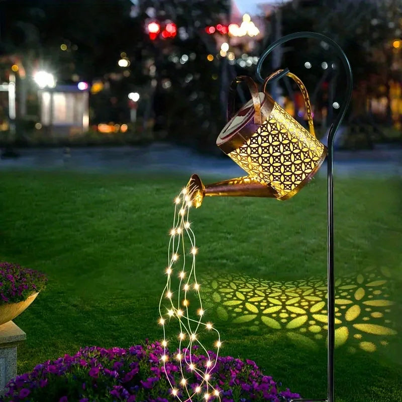 A vintage solar watering can garden light with a shepherd's hook illuminates a garden scene at night.