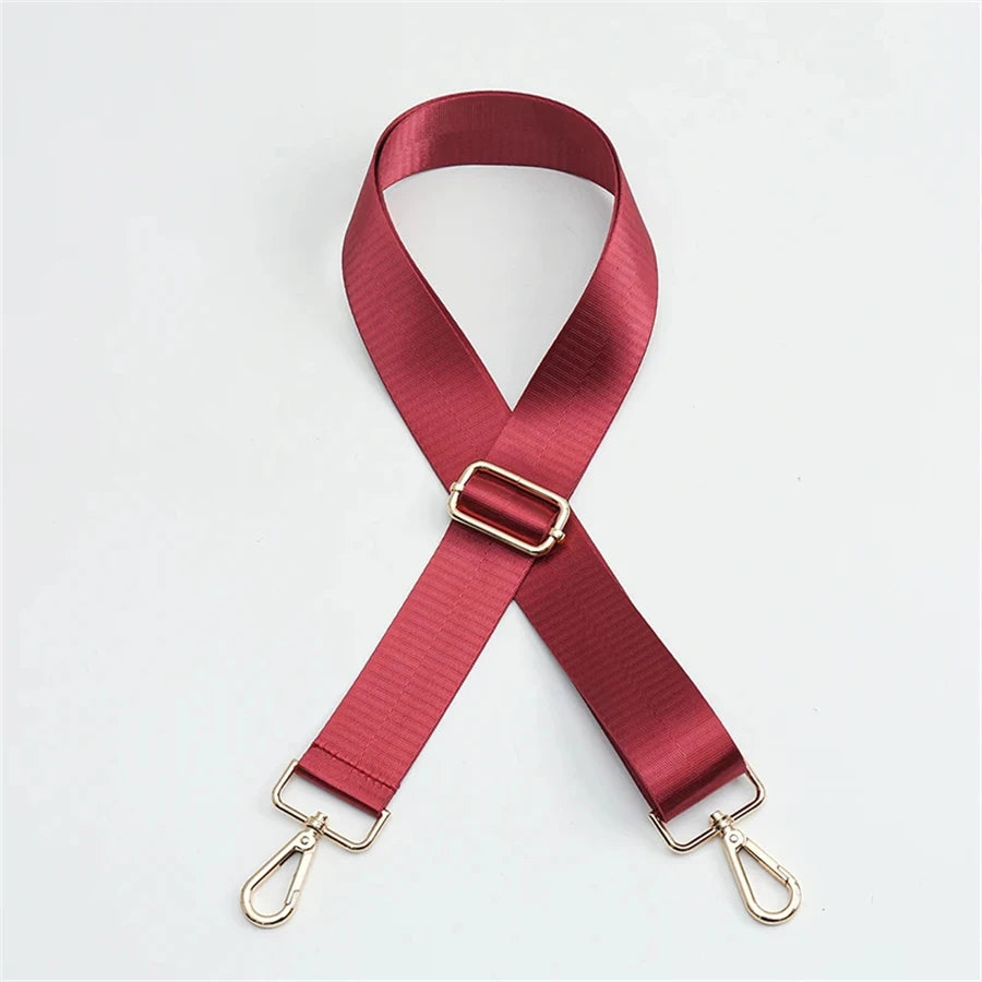 A maroon nylon bag strap with a gold buckle shown in an 'X' shape.