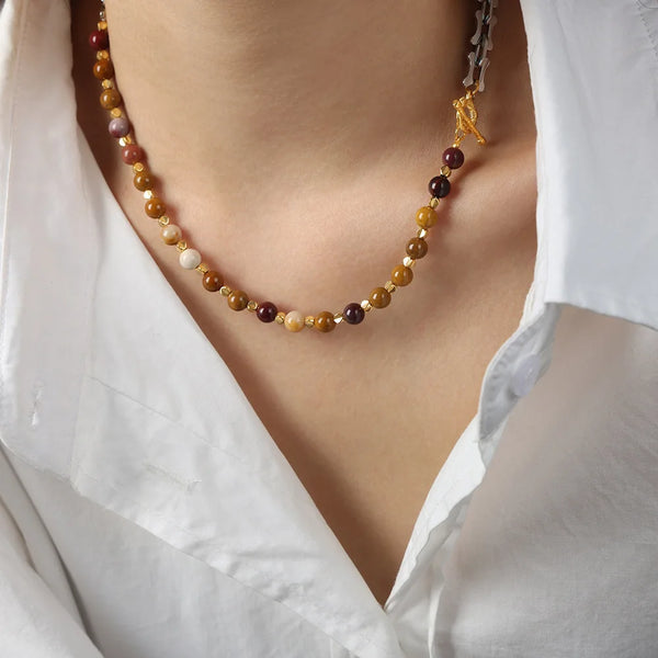 Rapprochement d'un collier en acier inoxydable artisanal avec de petites perles rondes ambre et violet foncé.