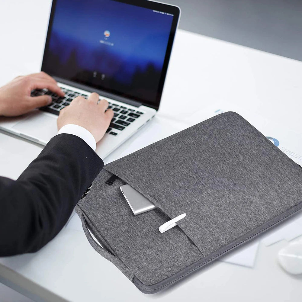 A person is using a laptop and holding a gray waterproof laptop sleeve with a handle on a white desk.