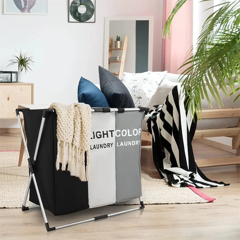 A foldable laundry basket with handles and sorting compartments in black, white, and gray is shown indoors.