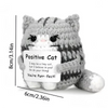A handmade crochet cat doll with a striped gray and white body and a positive message card.