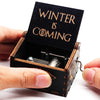 A hand is opening a vintage wooden music box with a lid engraved 'Winter is Coming' to reveal the mechanism.