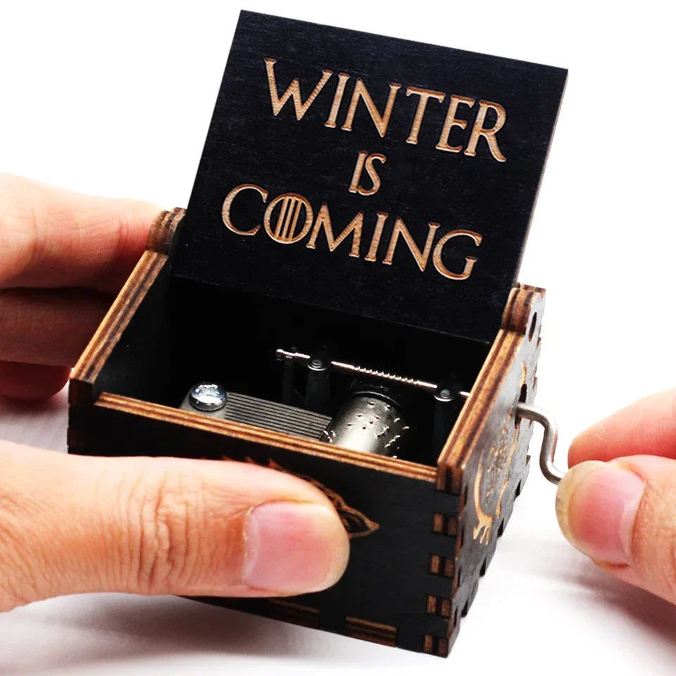 A hand is opening a vintage wooden music box with a lid engraved 'Winter is Coming' to reveal the mechanism.