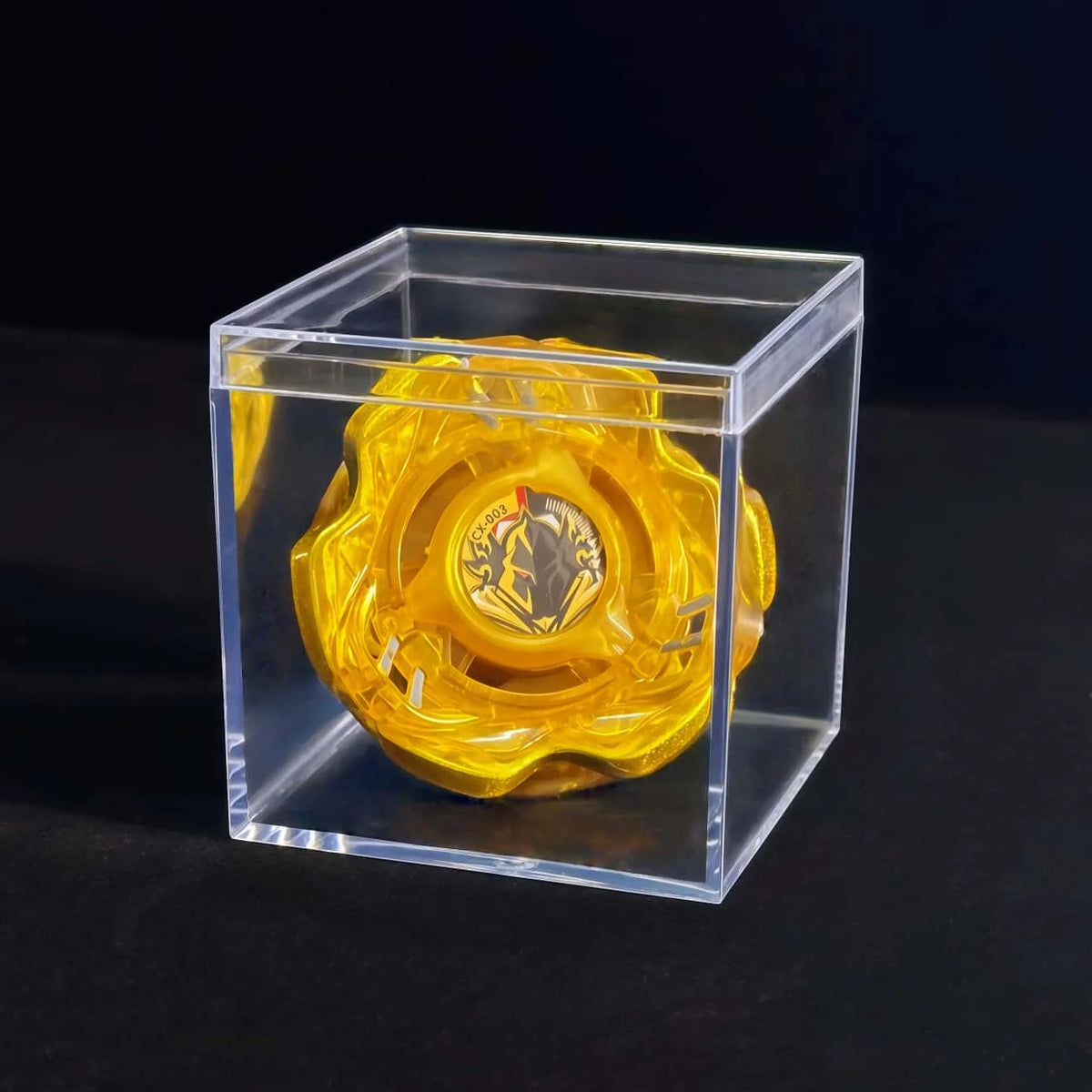 A yellow metal spinning top is displayed inside a clear acrylic box.