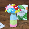 A colorful bouquet of felt and button flowers in various shades of pink, blue, yellow, and red displayed in a glass vase.