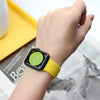 A hand is wearing a yellow silicone sport band on an Apple Watch, resting near a yellow surface and printed material.