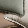 A close-up of a sage green boho fringe throw pillow cover with a natural linen texture resting on a beige cushion.