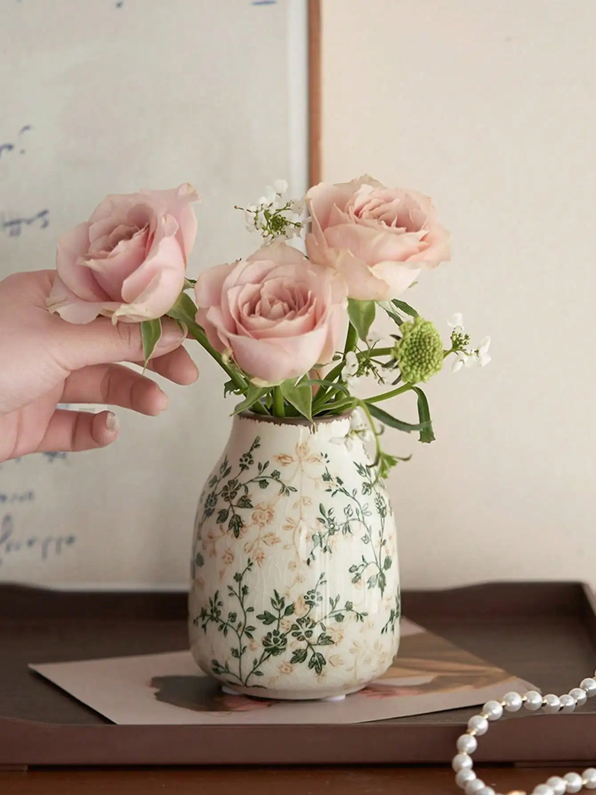 Eine Hand hält eine Vase mit rosa Rosen in einer handgefertigten Eis-gecrackten Keramikvase mit grünem Laub.