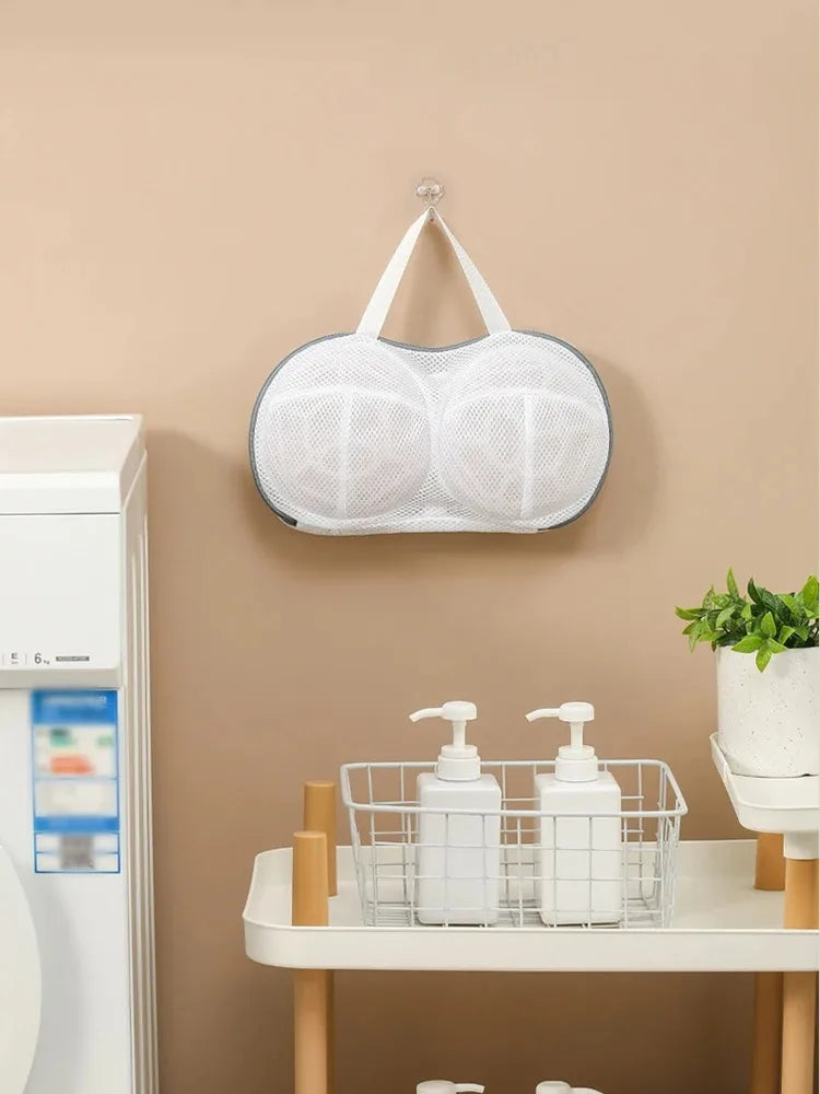 A white mesh laundry bag with a hanger is displayed on a wall, next to a washing machine.