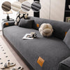 A gray anti-slip lamb fleece sofa mat is shown with decorative pillows and a cup on a modern sofa.
