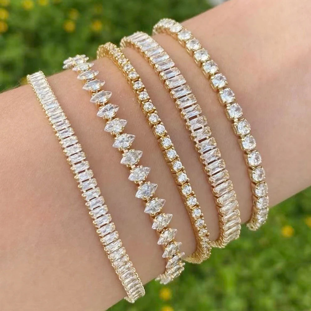Goldfarbene Tennisarmreifen mit klaren Diamant-Strohsteinen, gestapelt am Handgelenk.