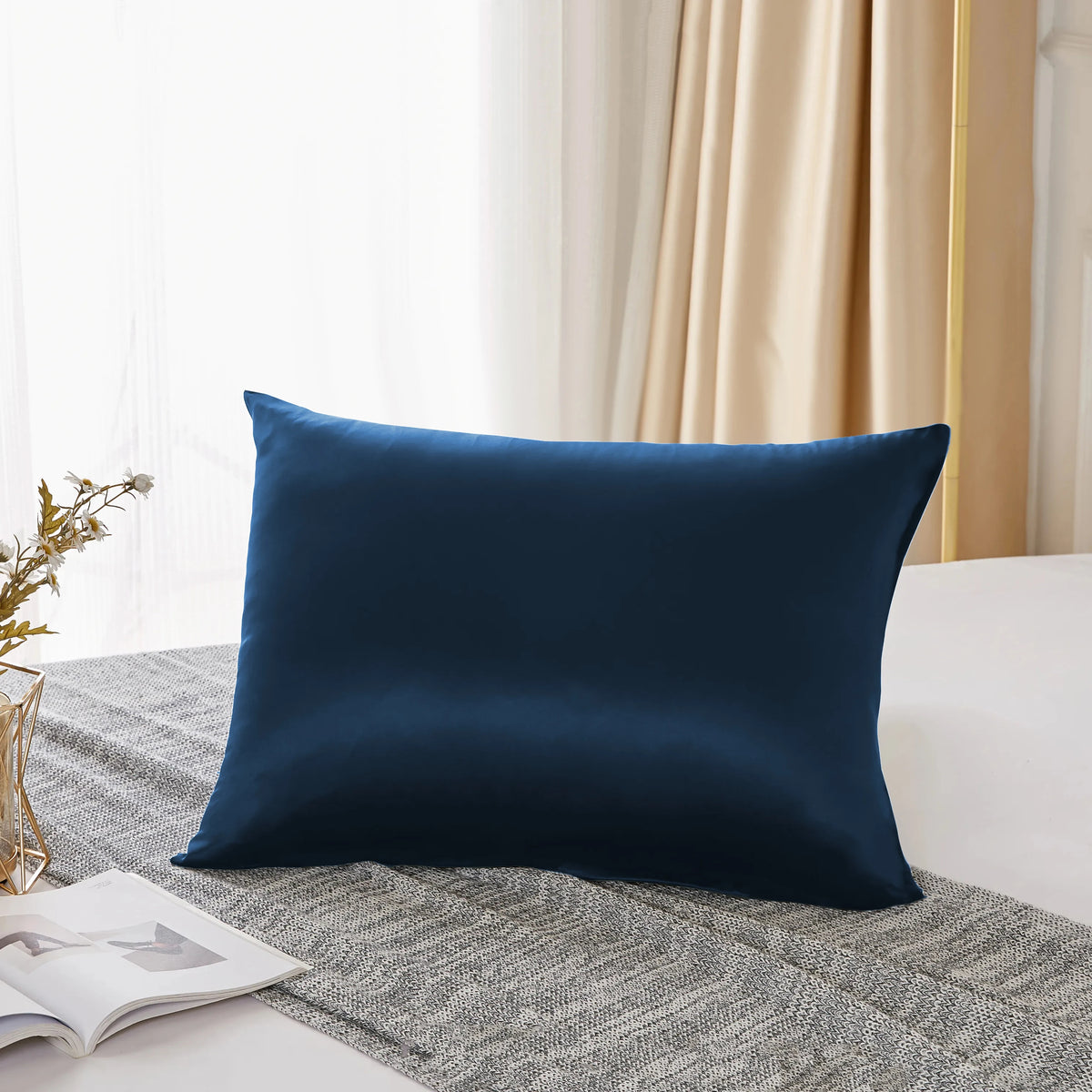 Housse de satin bleu marine foncé posée sur un tissu gris près d'une fenêtre avec des rideaux clairs.