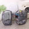 A black foldable laundry hamper with mesh netting is shown next to a white plastic storage bin and a washing machine.