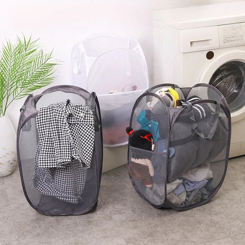 A black foldable laundry hamper with mesh netting is shown next to a white plastic storage bin and a washing machine.