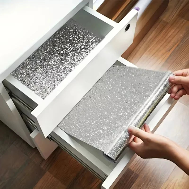 Hands are peeling and sticking an aluminum foil kitchen backsplash wall sticker onto a cabinet door.