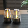 Two glass votive candles with flickering yellow flames resting on a dark surface.