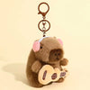 A brown capybara plush toy is holding a small acoustic guitar keychain.