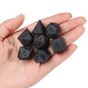 A hand holds a set of matte black polyhedral dice used for tabletop role-playing games.
