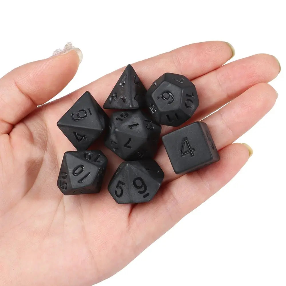 A hand holds a set of matte black polyhedral dice used for tabletop role-playing games.