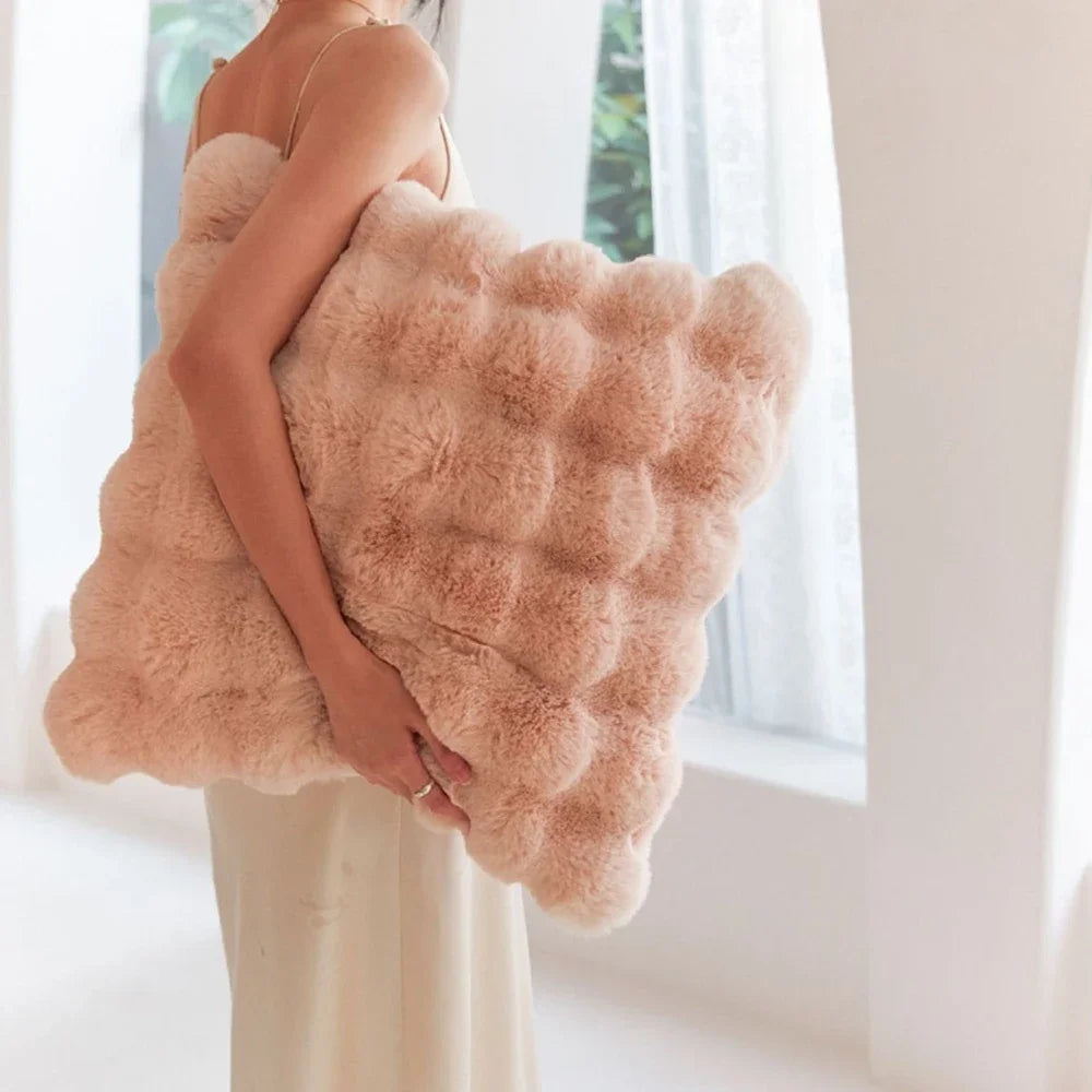 A person is holding a large, fluffy, light pink faux fur decorative pillow cover.