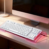 A pink acrylic ergonomic keyboard riser with a non-slip base is placed on a light desk next to a computer monitor.