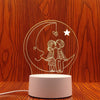 A white line drawing of a couple silhouette inside a crescent moon on a light pink lamp base.