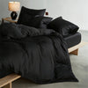 A black luxury mulberry silk duvet cover set displayed on a bed with a bedside lamp.