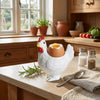 A white ceramic chicken egg cup with a cracked egg resting on it, displayed on a wooden table.