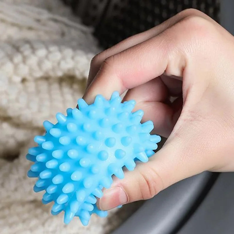 A hand holds a bright blue reusable laundry ball against a textured white fabric background.