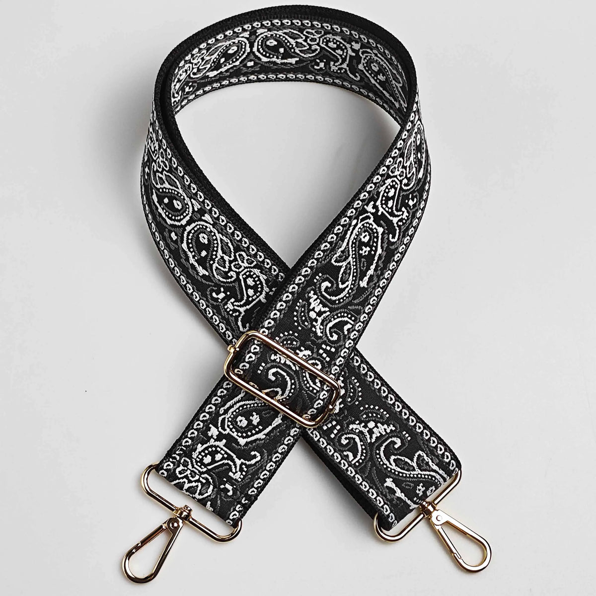 A black and white paisley jacquard bag strap with gold hardware shown diagonally.