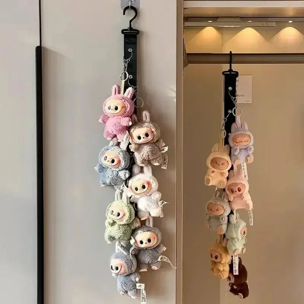 A wall-mounted display rack featuring several soft, fuzzy dolls in various pastel colors hanging by a chain.
