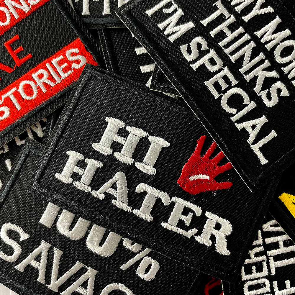 A close-up of black embroidered iron-on patches featuring text like HI HATER and 100% SAVAGE.