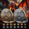 A dragon silhouette looms over two silver and gold metal dice cases, with various polyhedral dice scattered below.