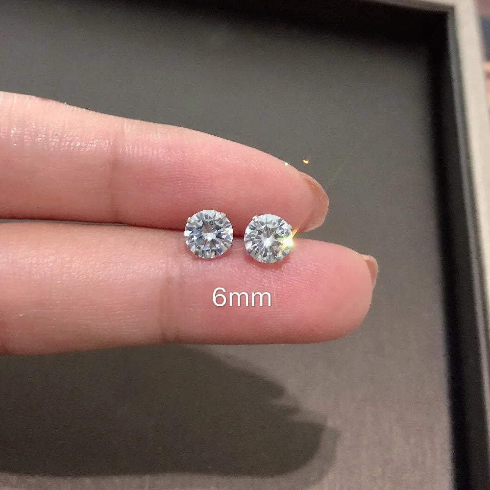 Une main tient une paire de minuscules clous d'oreilles en cristal CZ transparents sur un doigt, avec une mesure de 6 mm visi