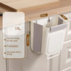 Weißer faltbarer Küchen- und Campingmülleimer hängt an einem Holzschrank mit Markierungen.