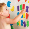 A toddler is interacting with a wall display of colorful EVA bath letters and numbers.