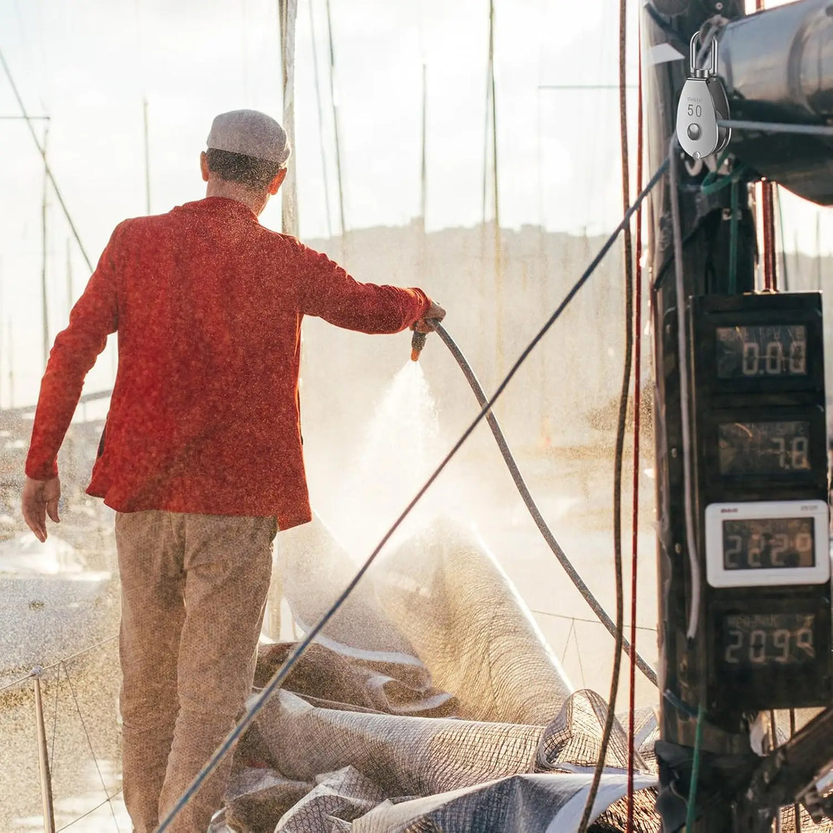 A person in a red jacket is operating a stainless steel swivel pulley system for a boat.