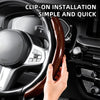 A hand is installing a glossy carbon fiber clip-on steering wheel cover onto a car's steering wheel.