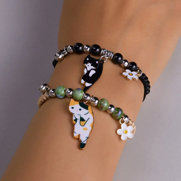 A black beaded bracelet featuring enamel charms of a cat and a flower on a person's wrist.