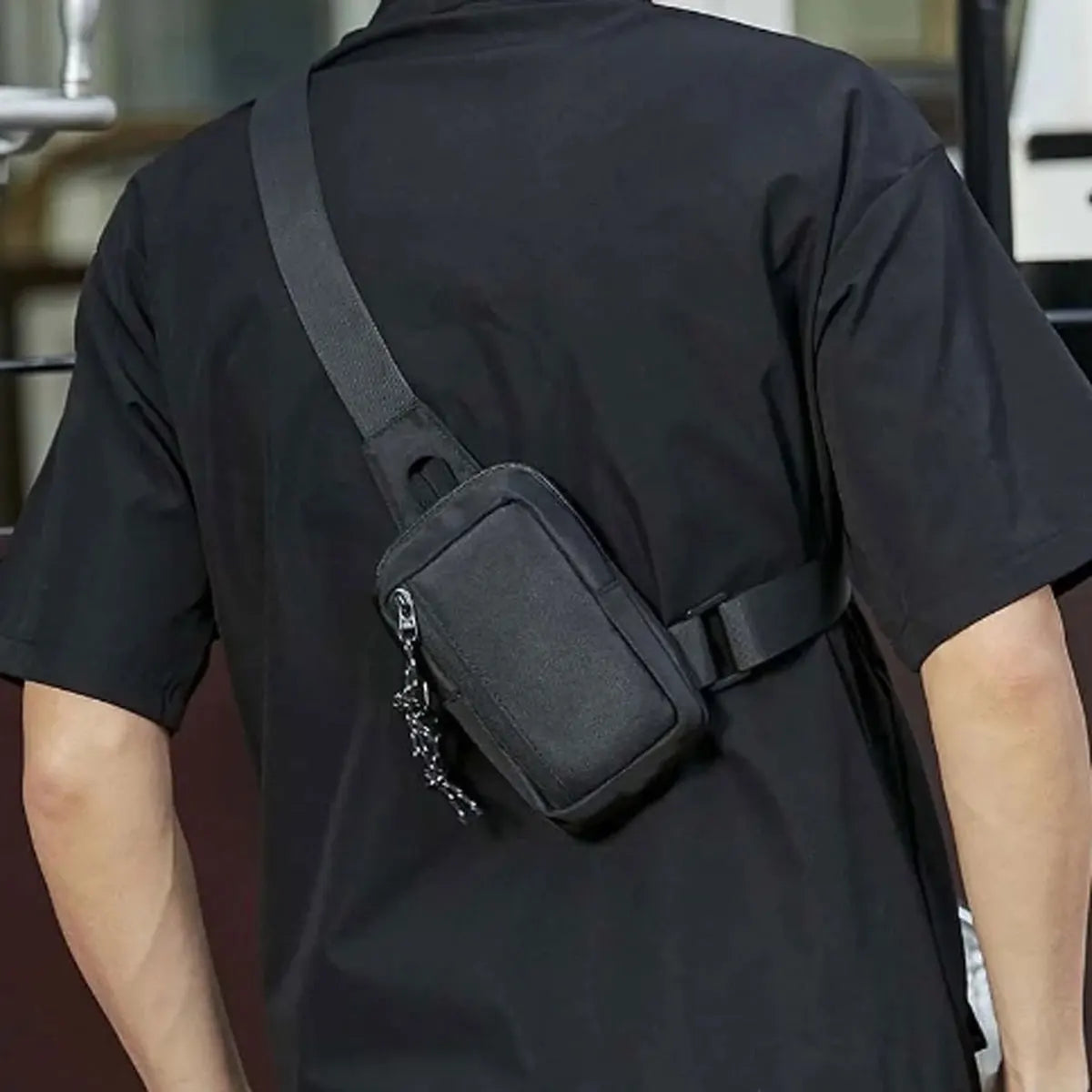 A person wearing a black short-sleeved shirt with a black canvas crossbody bag attached to the shirt.