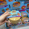 Eine Hand hält ein gelbes Squishy-Spielzeug mit bunten Perlen darin, verpackt in einer Box.