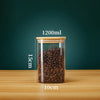 A glass storage canister filled with dark roasted coffee beans, featuring a bamboo lid and marked volume lines.