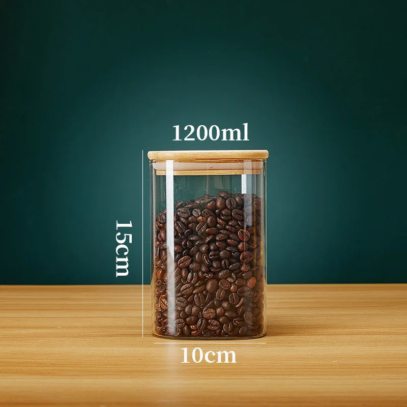 A glass storage canister filled with dark roasted coffee beans, featuring a bamboo lid and marked volume lines.