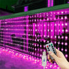 A hand holds a USB LED curtain light setup illuminating a window with vibrant pink and purple lights.