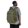 A man wearing a olive green tactical backpack with a MOLLE system standing against a white background.