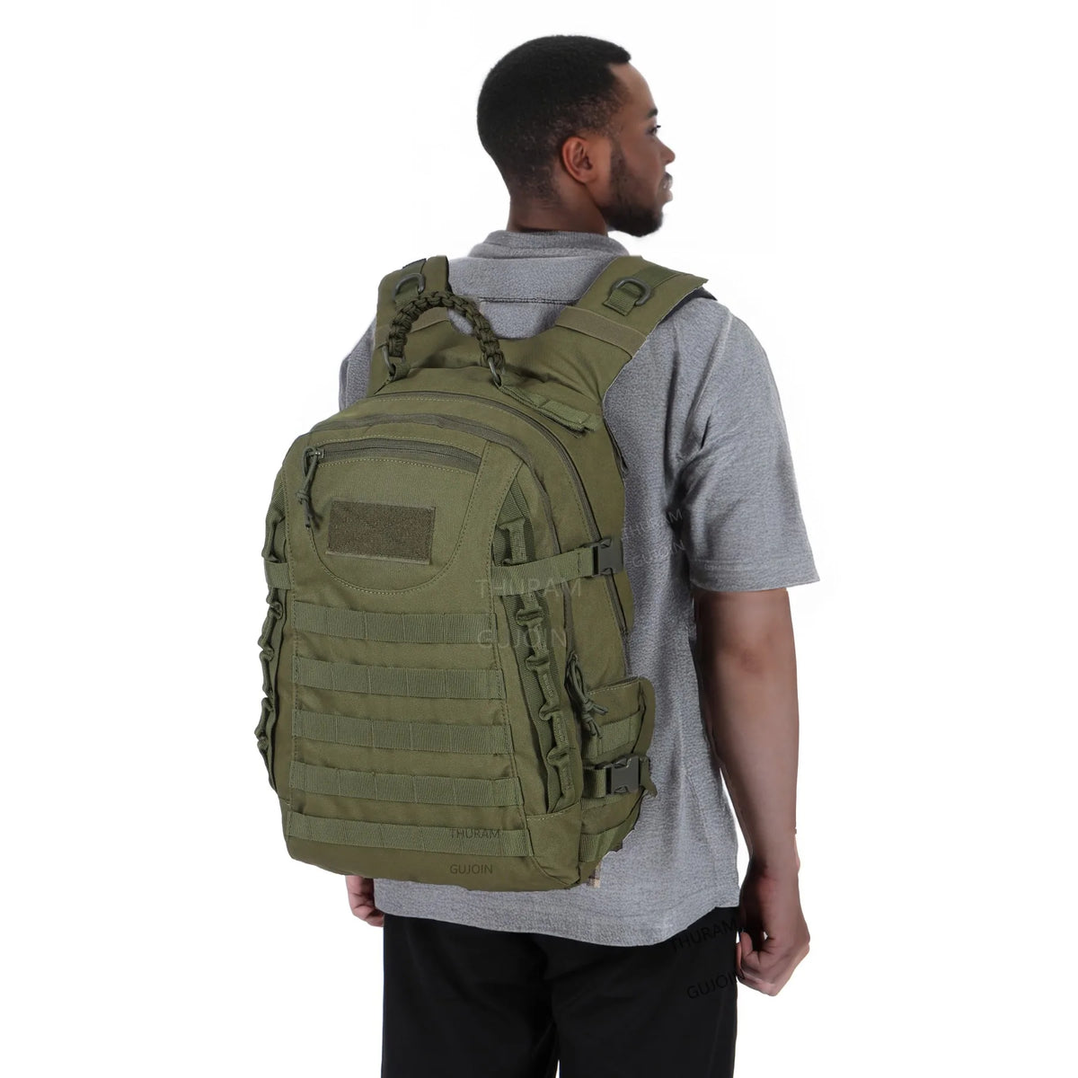 A man wearing a olive green tactical backpack with a MOLLE system standing against a white background.