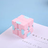 A pink infinity magic cube fidget toy resting on a white surface with text visible below.