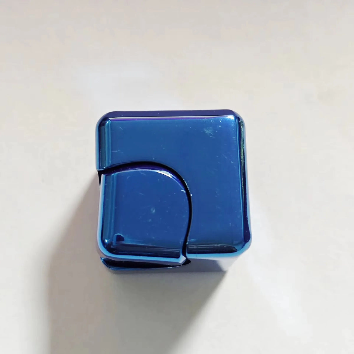 A small, rectangular blue metal fidget spinner cube resting on a white surface.